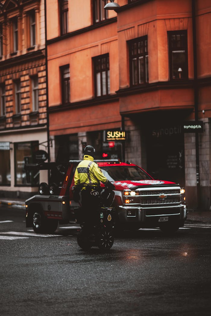 Urban setting with police patrol on Segway and a tow truck parked on a wet city street. Get Paid Top Dollar for Your Junk Cars In Calgary